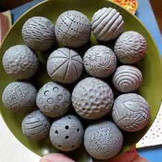 a person holding a green bowl filled with different sized and shaped balls on top of a table