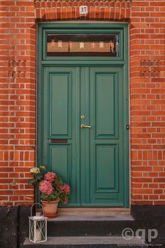 a green door with flowers in front of it on the side of a brick building