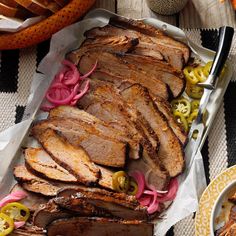 a platter with sliced meat, onions and peppers next to other foods on a table