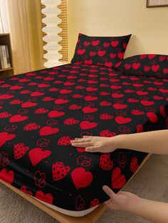 a person reaching for a bed with red hearts on it and black bedspread