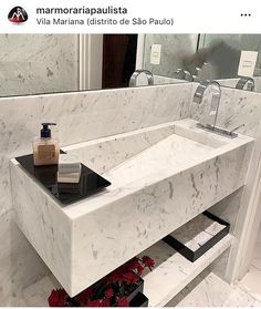 a white marble sink in a bathroom with red flowers on the counter and mirror behind it