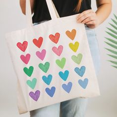 a woman holding a white bag with hearts painted on the front and sides in different colors