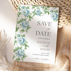 a white and blue floral wedding save the date card on a table with a basket