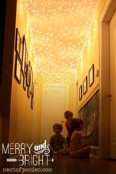 two children sitting on the floor in front of a door with christmas lights hanging from the ceiling