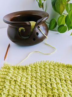 a green knitted dishcloth next to a brown crochet pot with a hook