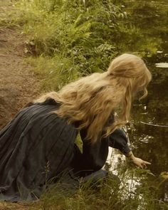 a woman kneeling down next to a body of water