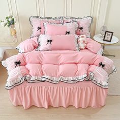 a bed with pink sheets and black bows on the comforter is in front of a white wall