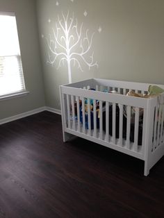 a white crib in the corner of a room with a tree painted on the wall