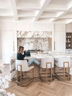 a woman sitting at a kitchen island with marble counter tops and white chairs in front of her