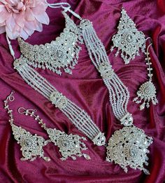 an assortment of bridal jewelry on a pink satin surface with a flower in the background