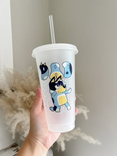 a hand holding a plastic cup with a straw in it and an image of a cartoon character on the side