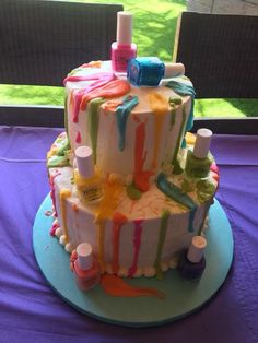 a multi - tiered cake decorated with colorful icing and nail polish on a purple table cloth