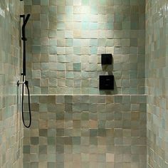 a tiled shower with black fixtures and green tiles on the walls, along with a white toilet