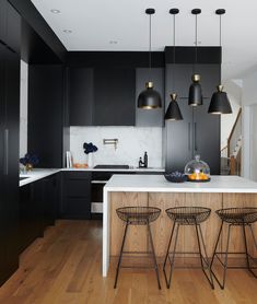 a kitchen with black cabinets and stools next to an island in front of the sink