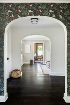 an archway leading into a living room with floral wallpaper on the walls and hardwood floors