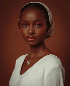 a woman wearing a white dress and a head scarf on top of her head is looking at the camera