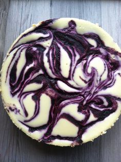 a white and purple cake sitting on top of a wooden table next to a knife