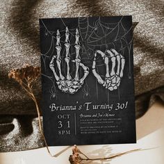 a black and white halloween party card with skeleton hands on it, sitting on a table