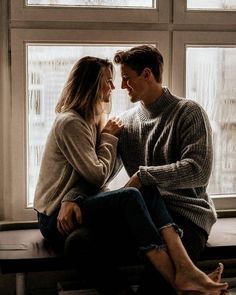 a man and woman sitting next to each other on a window sill looking at each other