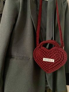 a red heart shaped purse hanging on a coat rack in front of a gray jacket