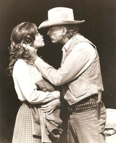 an old black and white photo of two people dressed in western clothing, one holding the other's head