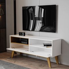 a white entertainment center with wooden legs and a black painting on the wall behind it