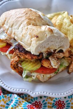 a chicken sandwich with lettuce and tomato on a plate next to potato chips