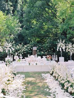 an outdoor wedding setup with white flowers and greenery on the grass, surrounded by trees