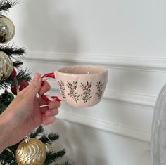 a person holding a cup in front of a christmas tree with ornaments on the wall