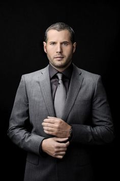 a man in a suit and tie is posing for a photo with his hands on his chest