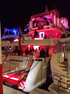 several boats are docked at night with people standing on the deck and one boat is white