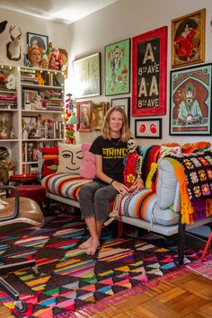 a woman sitting on a couch in a room with lots of pictures and rugs