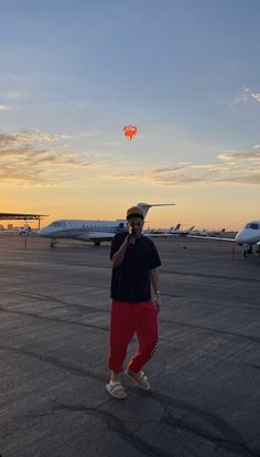 a man standing on an airport tarmac with a hot air balloon in the sky