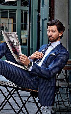 a man in a suit sitting on a chair reading a newspaper