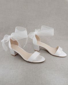 a pair of white wedding shoes with a bow on the toe and heels in satin