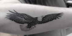 an eagle tattoo on the arm is shown in black and grey colors, with its wings spread