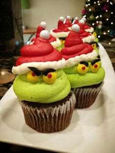 three cupcakes with green frosting and santa hats on them sitting on a white plate