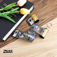 a camera keychain sitting on top of a wooden table next to a book