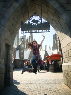 a woman jumping into the air in front of an entrance to hog's castle