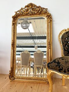 an ornate gold framed mirror sitting on top of a wooden floor next to a chair