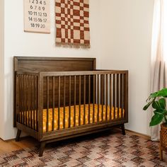 a wooden crib in the corner of a room next to a potted plant