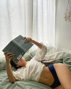 a woman laying on top of a bed holding a book in her hand and reading it