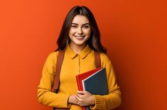 a woman in yellow shirt holding two books and smiling at the camera with orange background