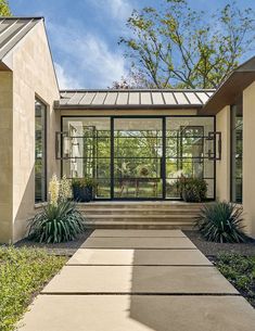 an entry way to a house with glass doors and plants on the side of it