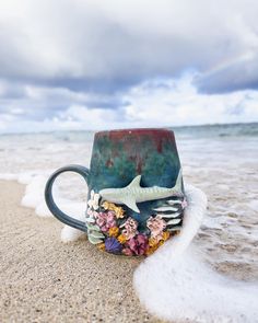 a coffee cup sitting on top of a sandy beach next to the ocean under a cloudy sky