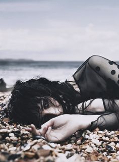 a woman laying on top of a rocky beach next to the ocean with her hands under her face