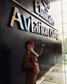 a woman is standing in front of the entrance to an aviation college building with her hand up