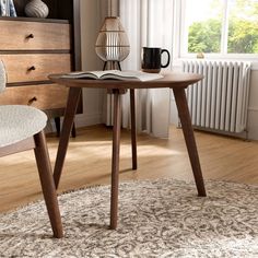 a wooden table with a book on top of it next to a chair in front of a window