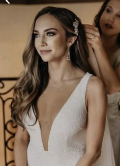 a woman in a white dress getting her hair combed by another woman with long hair