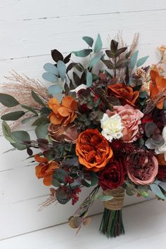 a bouquet of flowers is sitting on a white surface with greenery and dried leaves